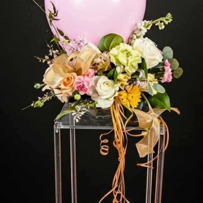 Pink balloon centerpiece with pastel flowers and ribbons in a clear vase on a tall stand