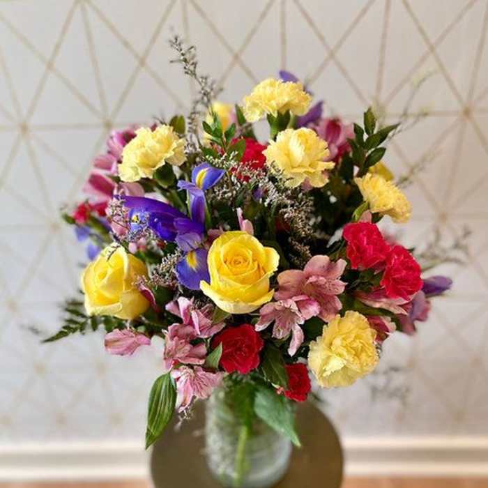 Mixed bouquet of roses, carnations, and purple flowers in a glass vase