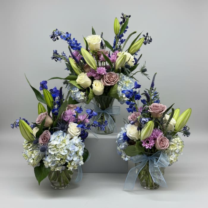 Three pastel floral arrangements in glass vases with blue ribbon bows