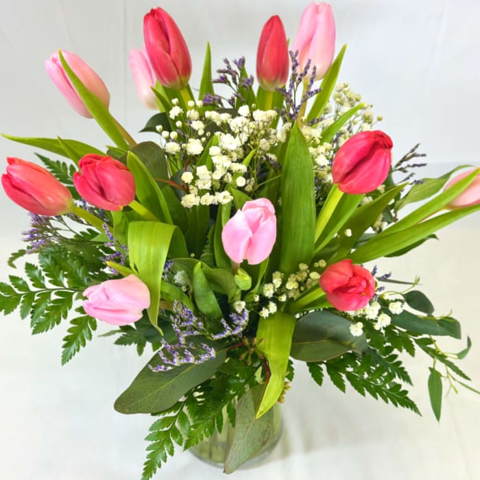Arrangement of pink and red tulips with white filler flowers in a clear glass vase