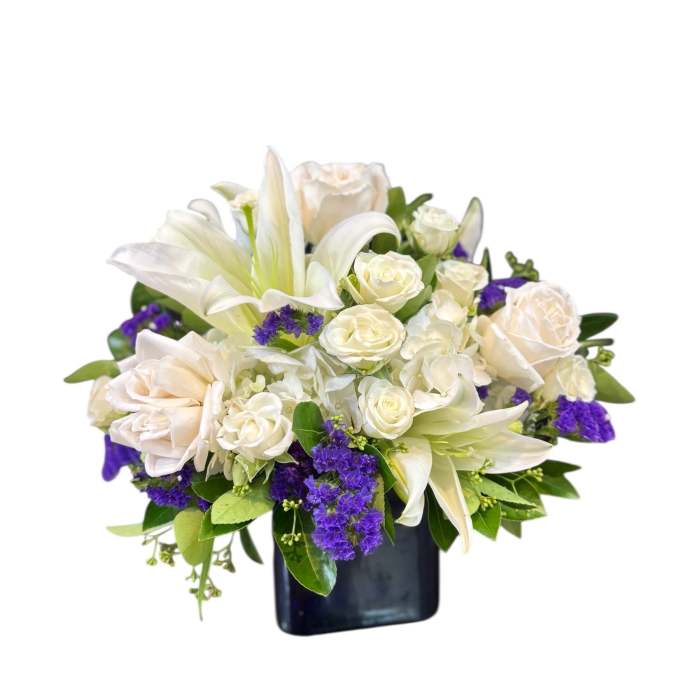 White lilies and roses arranged in a dark vase with purple accents