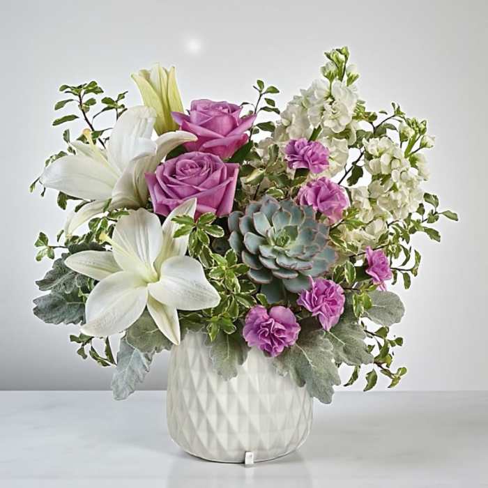 Pink roses and white lilies in a white vase with a succulent accent