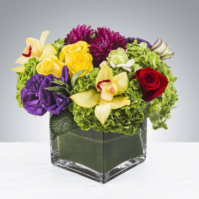 Colorful mixed bouquet in a square glass vase with roses and orchids