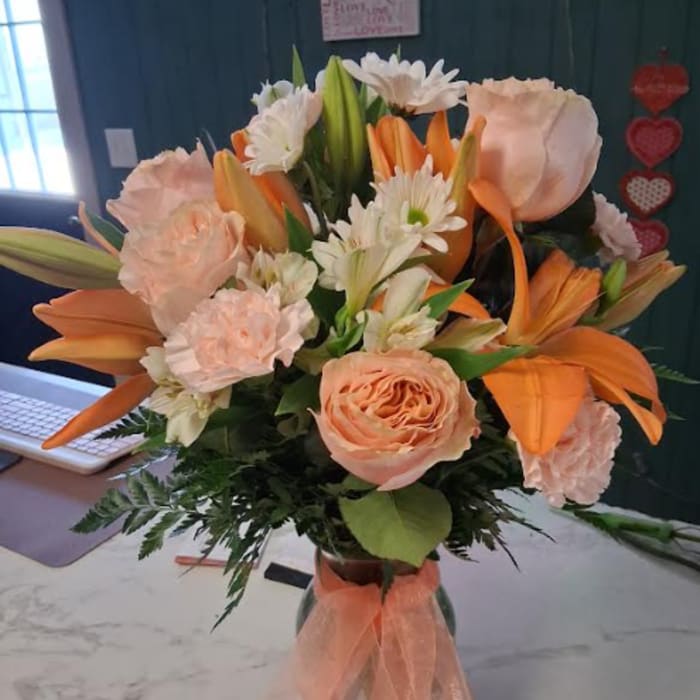 Peach and orange bouquet with lilies, roses, and white daisies in a glass vase
