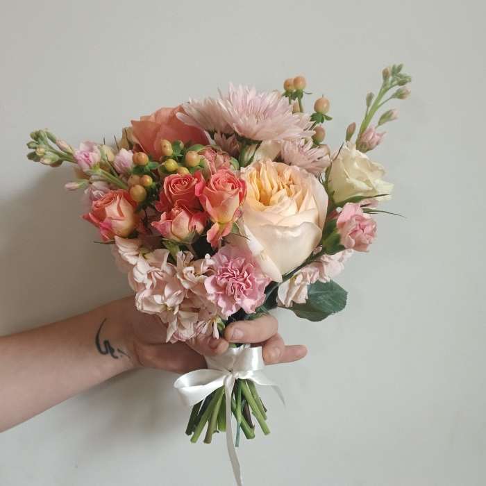 Handheld bouquet of pink and cream roses with pale blooms and a white ribbon