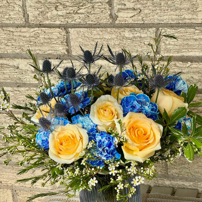 Yellow roses and blue carnations in a glass vase