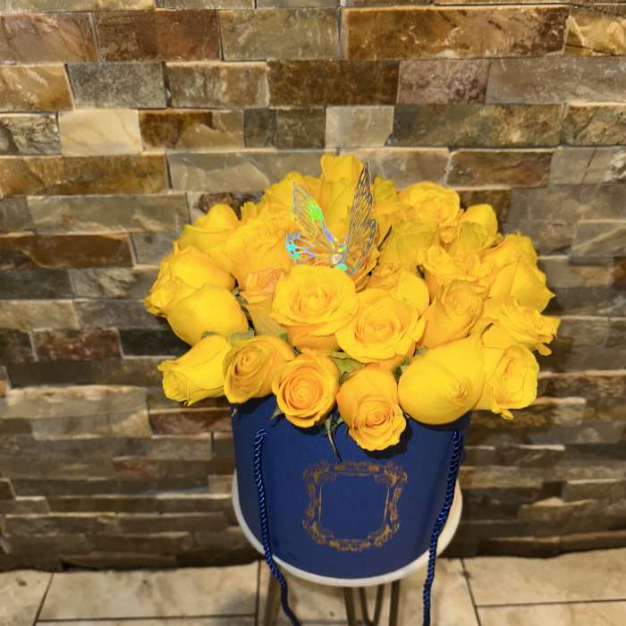 Yellow roses arranged in a blue hatbox with a butterfly pick