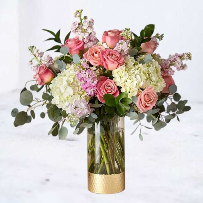 Pink roses and white hydrangeas in a tall glass vase with a gold base