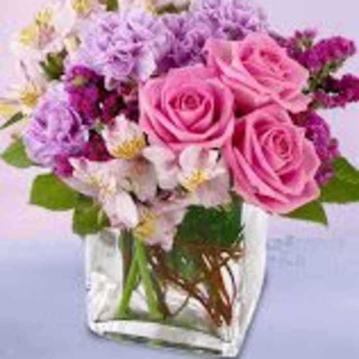Pink roses and purple flowers arranged in a clear square vase