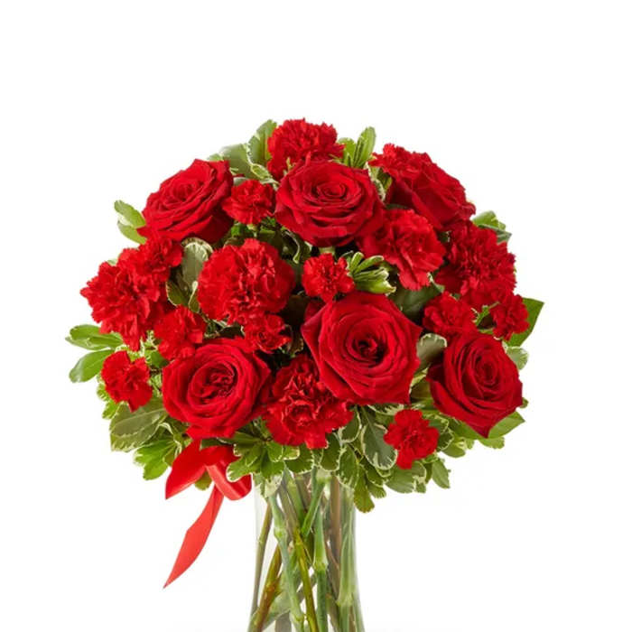 Red roses and carnations in a clear glass vase with a red ribbon