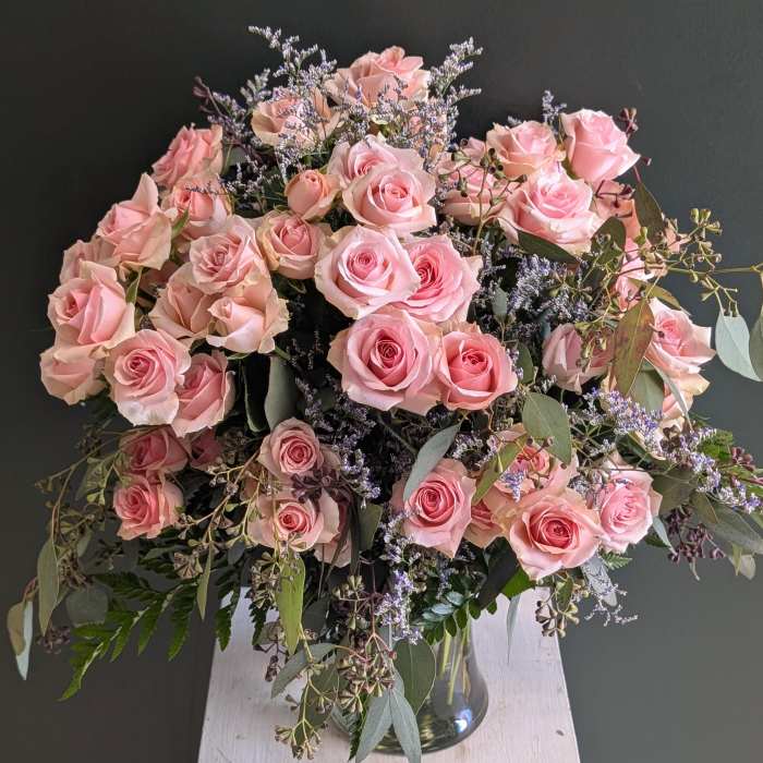 Large arrangement of pink roses with trailing foliage in a clear glass vase