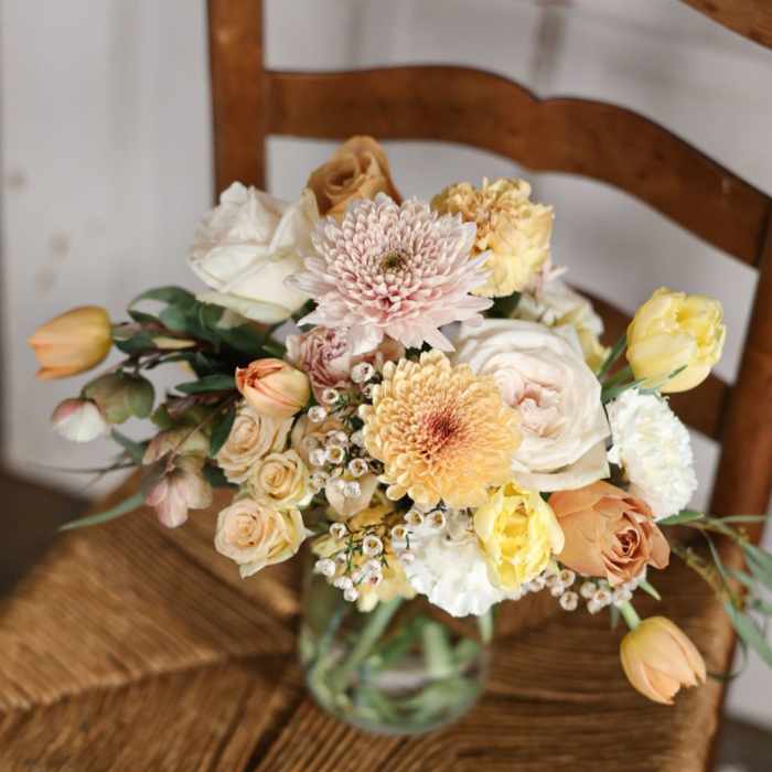 Mixed pastel bouquet in a glass vase on a wooden chair