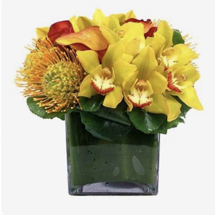Yellow orchids and orange-red tropical flowers in a square glass vase