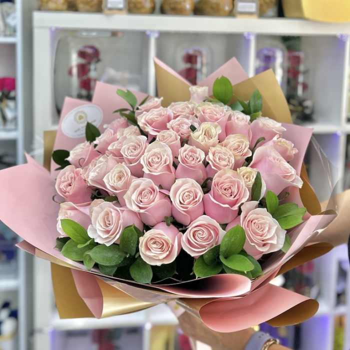 Large hand-tied bouquet of light pink roses wrapped in pink and tan paper