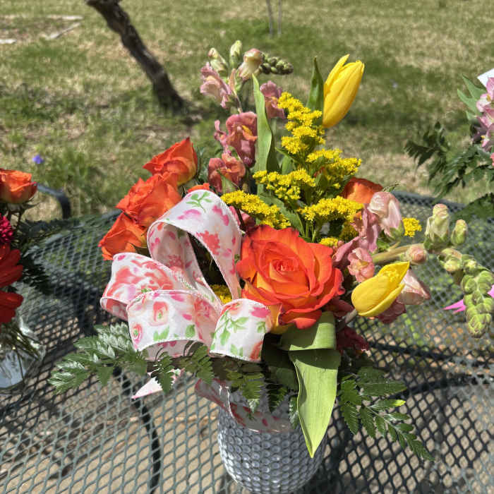 Bouquet of orange roses, yellow tulips, and pink snapdragons in a silver vase
