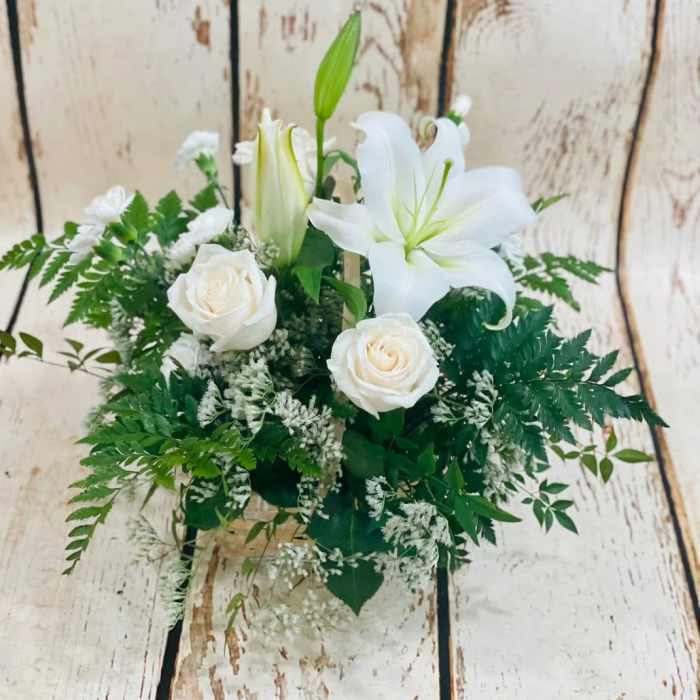 White lilies and roses arranged with greenery in a basket