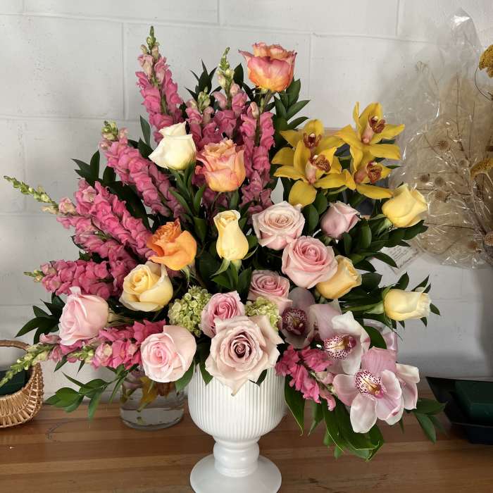 Mixed bouquet of pink, yellow, and peach flowers in a white vase.
