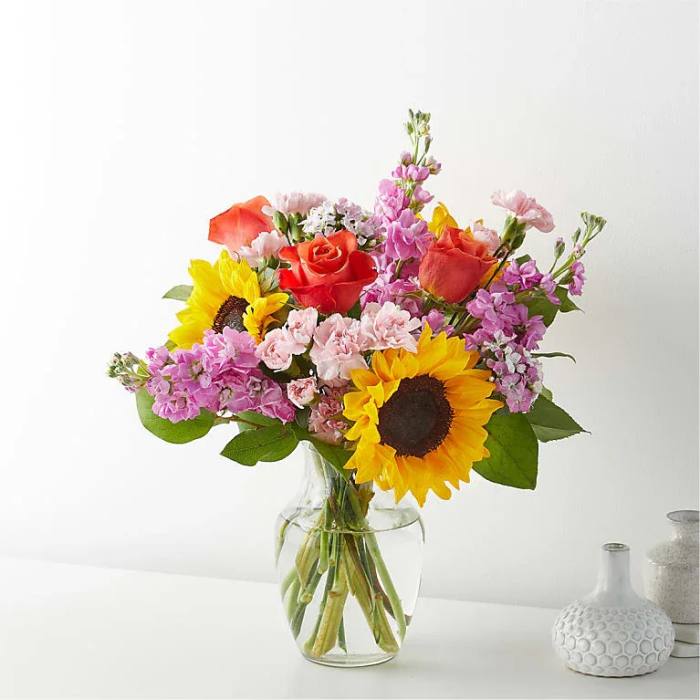 Mixed bouquet of sunflowers, roses, and pink blooms in a clear glass vase