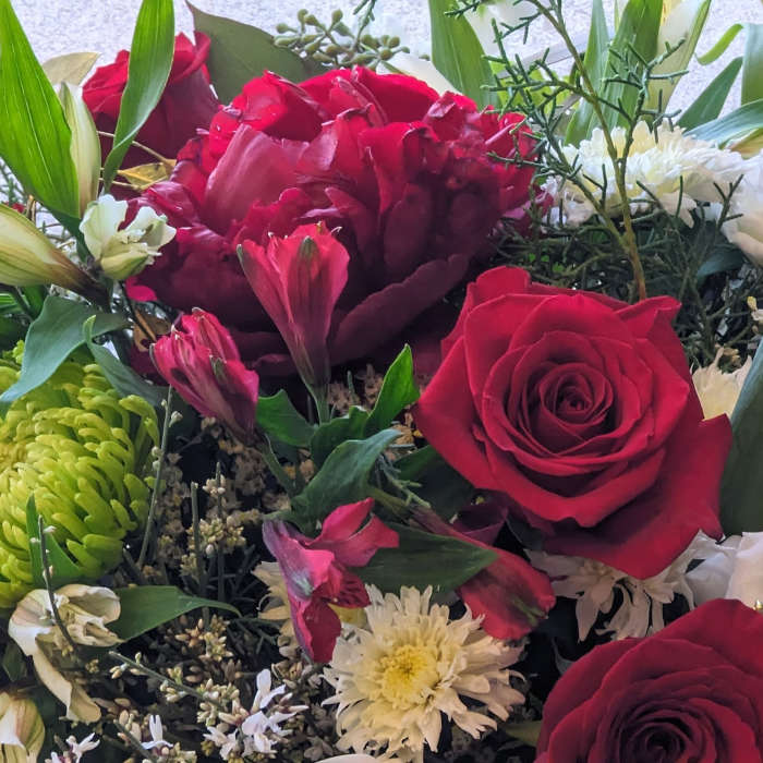 Mixed arrangement of red roses, red peony, and white and green chrysanthemums with accent blooms.