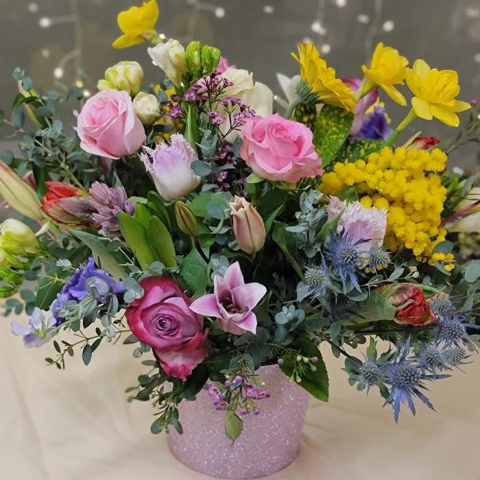 Mixed bouquet of pink, yellow, and purple flowers in a glittery vase