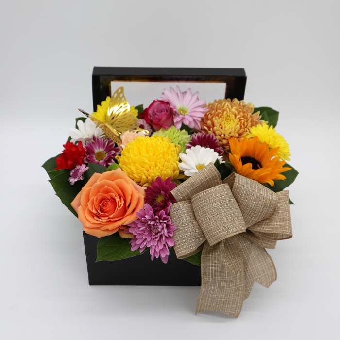 Mixed flowers arranged in a black gift box with a large tan bow