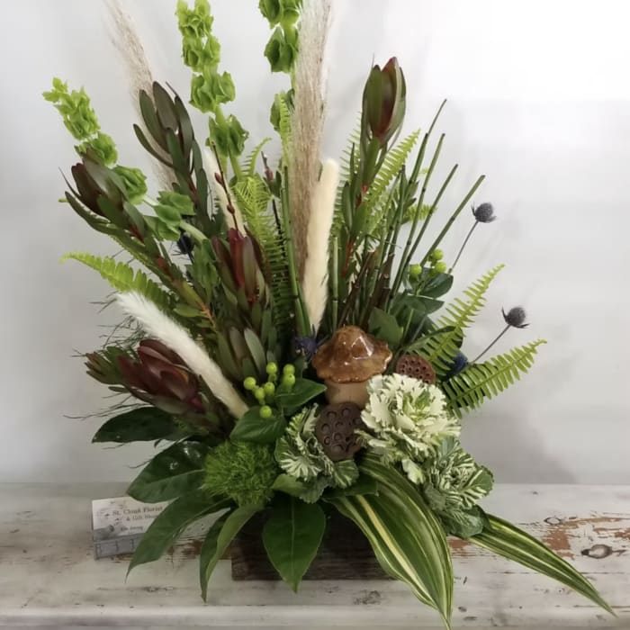 Tall green floral arrangement with tropical foliage and cream accents in a low container
