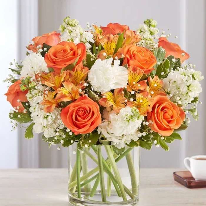 Orange roses and white flowers arranged in a clear glass vase