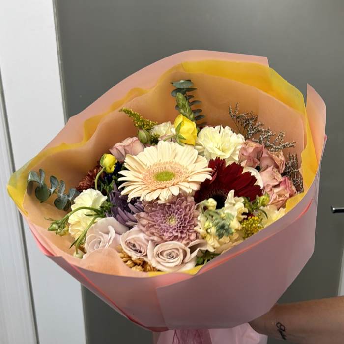 Hand-tied bouquet of mixed pastel flowers wrapped in pink and peach paper