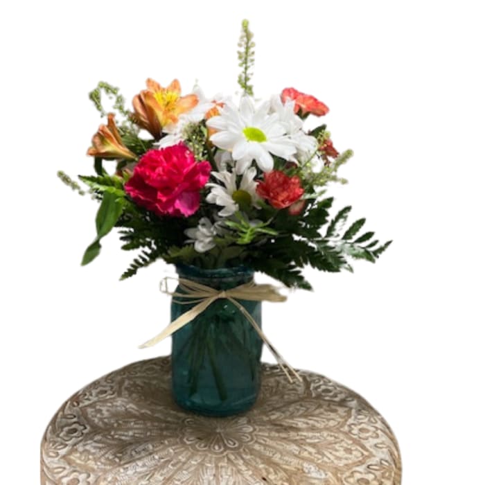 Mixed bouquet of daisies, carnations, and lilies in a blue glass vase