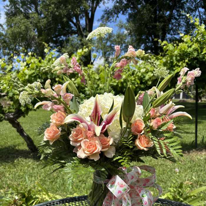 Peach roses and lilies in a glass vase with a floral ribbon