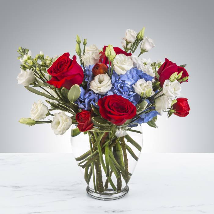 Red roses and white blooms arranged with blue hydrangeas in a glass vase