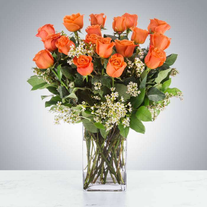 Orange roses in a clear glass vase with small white filler flowers