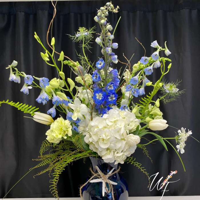 Tall blue and white floral arrangement in a dark vase