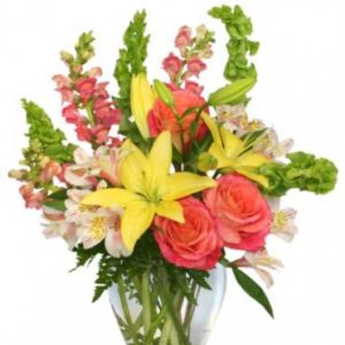 Bouquet of yellow lilies, pink roses, and snapdragons in a glass vase