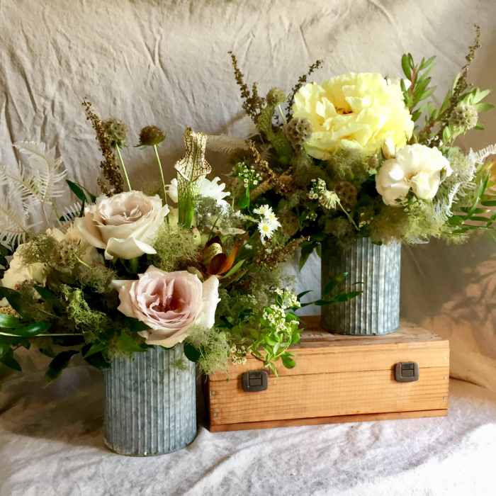Two floral arrangements in ribbed metal vases with pale roses and yellow blooms