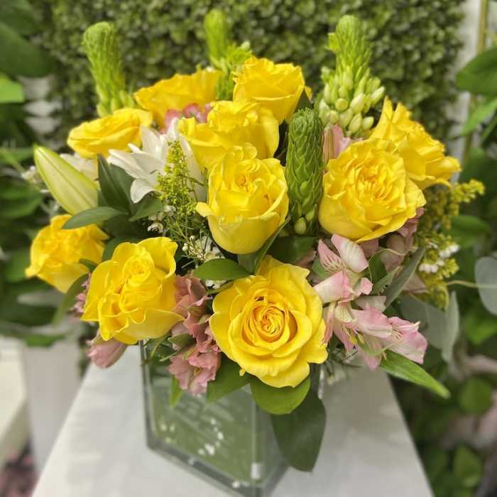 Yellow rose and pink alstroemeria arrangement with white lilies in a square glass vase