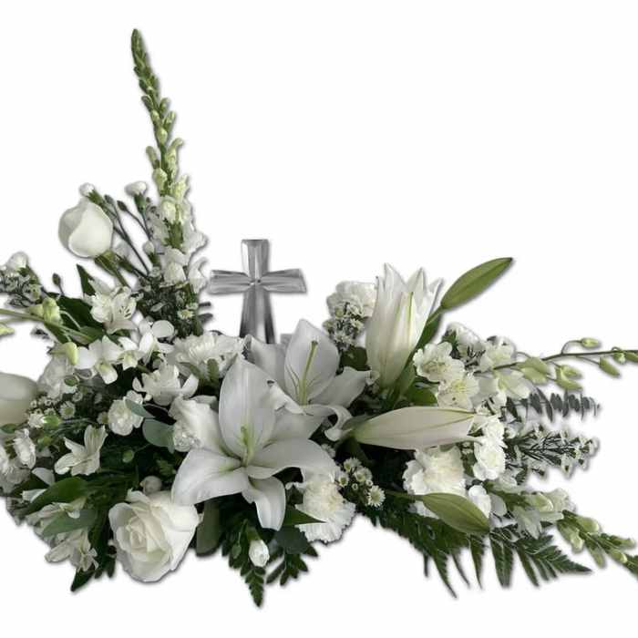 Low white floral spray with lilies, roses, and a central silver cross accent