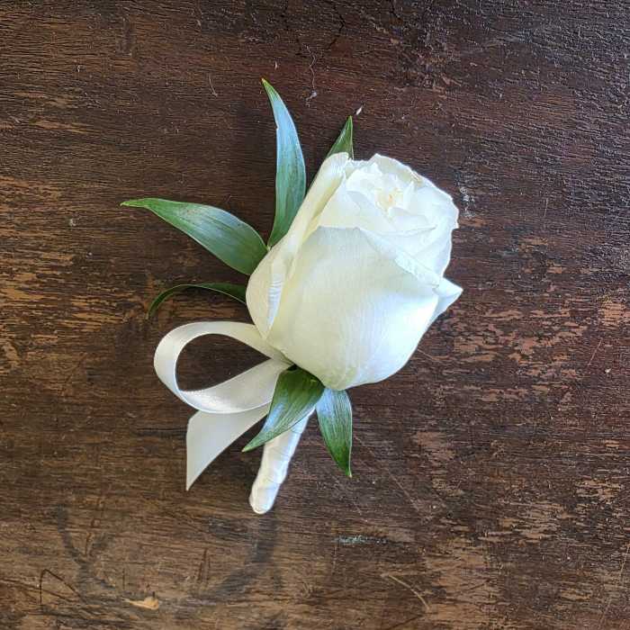 White rose boutonniere with green leaves and a white ribbon