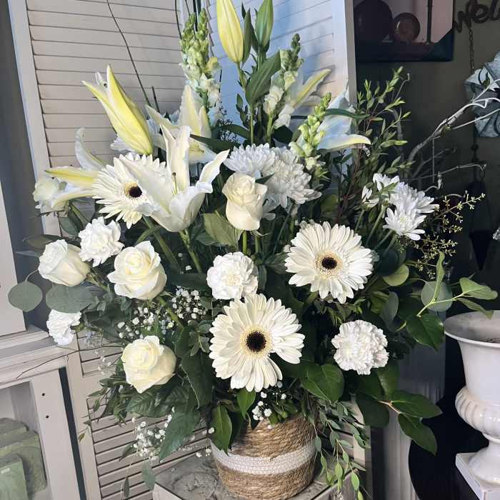 White floral arrangement with lilies, roses, and daisies in a woven vase