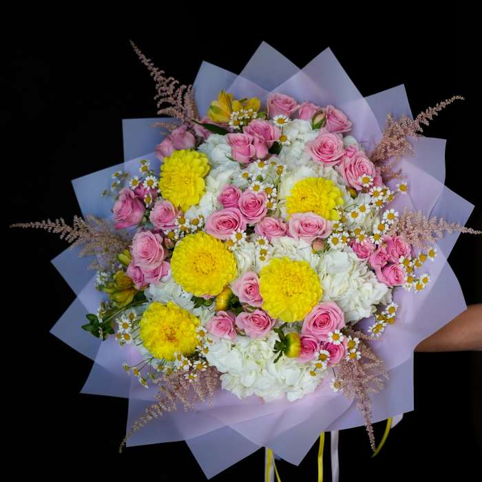 Bouquet of pink roses, yellow blooms, and white flowers wrapped in lavender paper
