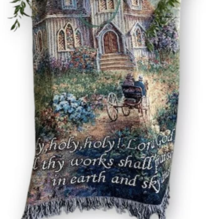 Religious tapestry blanket with church scene topped by white lilies and red roses with greenery.