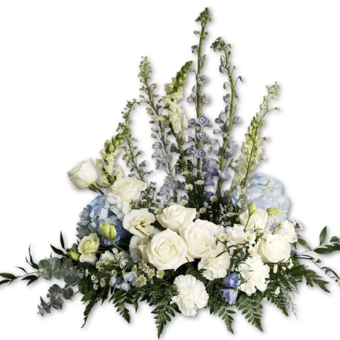 Large white and pale blue floral arrangement with roses, hydrangeas, and tall delphinium spikes