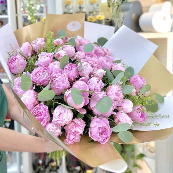 Large hand-tied bouquet of pink peonies wrapped in white and gold paper