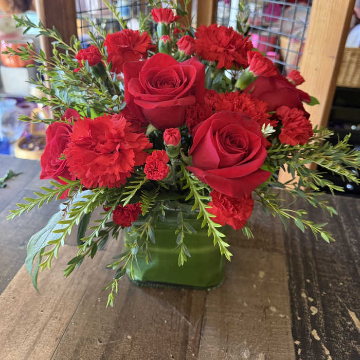 Red roses and carnations arranged in a green glass vase