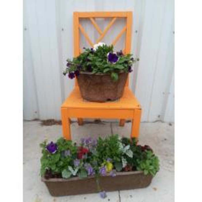 Two brown planters of mixed blooming plants displayed on and in front of an orange chair outdoors