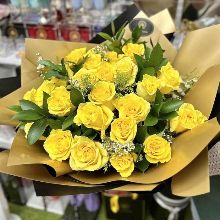 Hand-tied bouquet of bright yellow roses wrapped in gold and black paper.