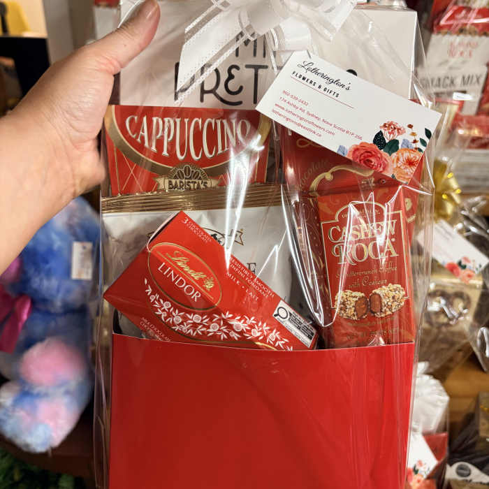 Red gift bag of cappuccino and chocolates wrapped in cellophane with a white bow.