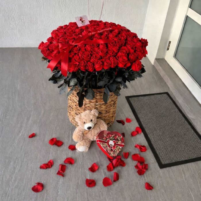 Basket of red roses with heart balloons, teddy bear, and candy box