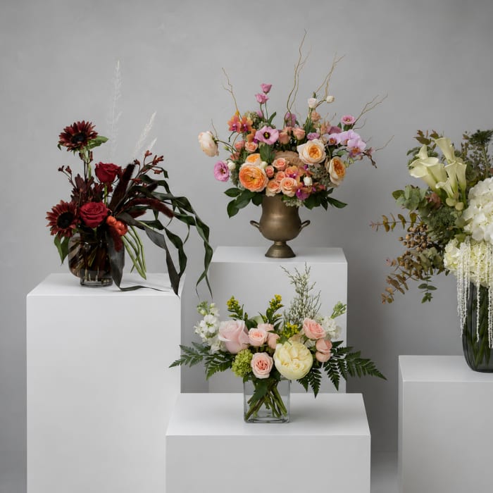 Four floral arrangements on white pedestals in glass and metal vases