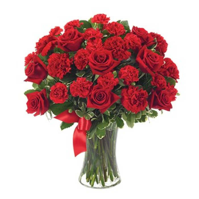 Red roses and carnations in a clear glass vase with a red ribbon